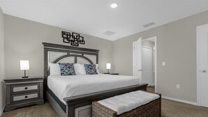 Quarto com uma cama grande, duas mesas de cabeceira, um banco e uma porta.