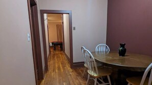 Un couloir au plancher de bois menant à une salle à manger équipée d’une table et de chaises.