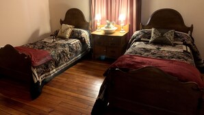 Une chambre avec deux lits en bois, une table de chevet avec une lampe et une fenêtre avec des rideaux.