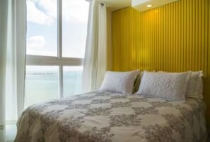 A bedroom with a large window, a bed with a floral bedspread, and a yellow wall.