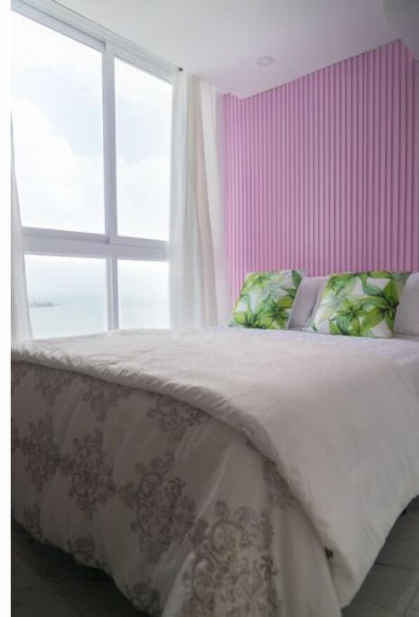 A bedroom with a large window, a bed with floral bedding, and a pink headboard.