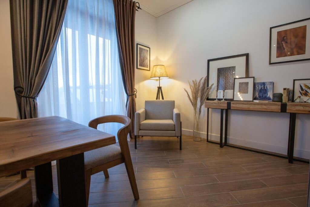 Un soggiorno moderno con un tavolo da pranzo in legno, una poltrona grigia e una lampada da terra. Alle pareti sono presenti opere d'arte incorniciate e un tavolino con oggetti decorativi.