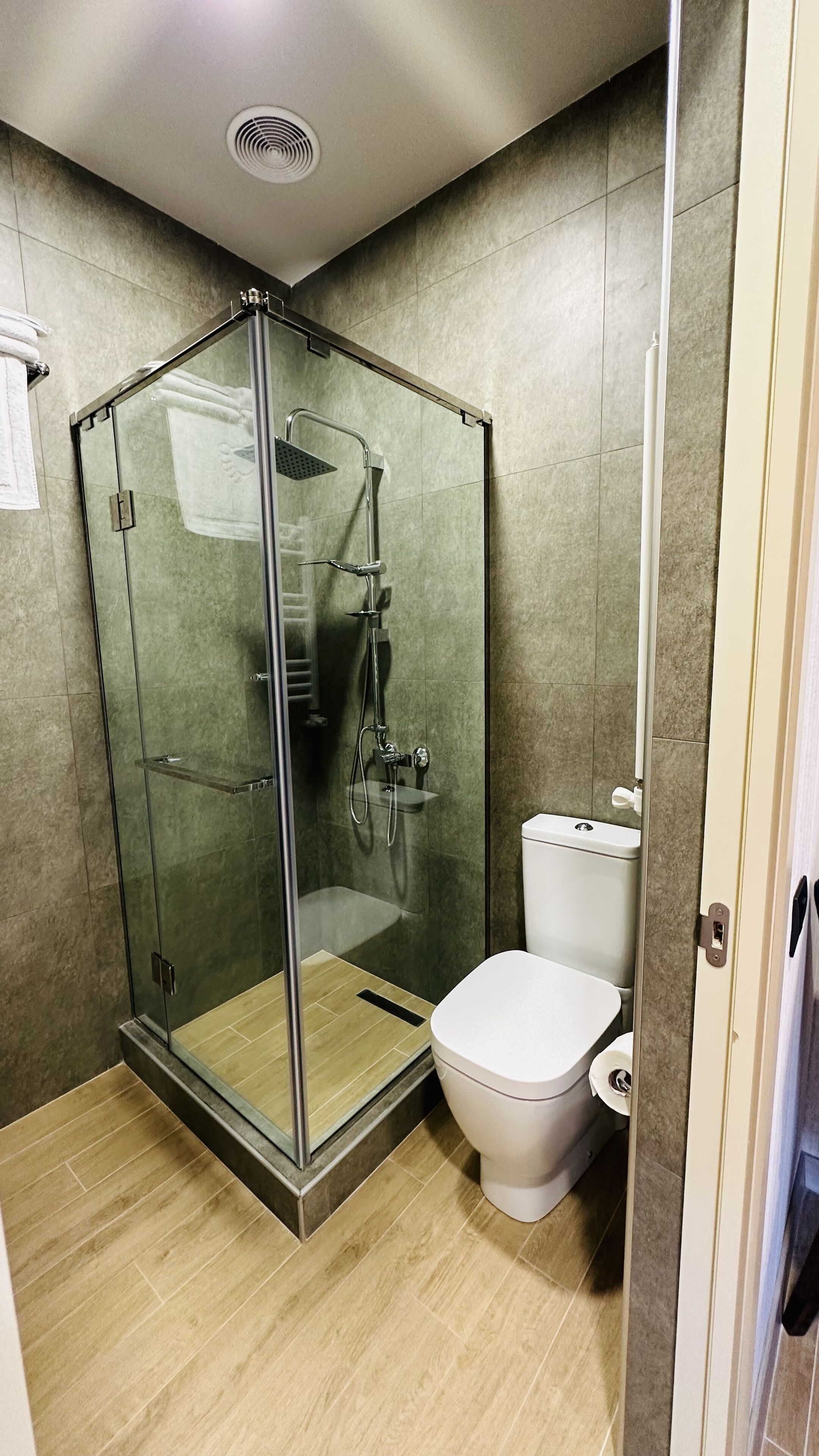 Une salle de bain moderne avec une douche à parois de verre, des toilettes blanches et un sol carrelé de couleur beige.