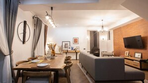 A modern living space with a dining area, sofa, fireplace, and flat-screen TV mounted on a brick wall. - Marrone Hotel Tsaghkadzor (Tsaghkadzor)