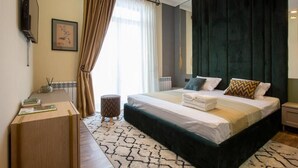 A hotel room with a bed, a desk, a chair, a small round table, a TV, and a window with curtains. - Marrone Hotel Tsaghkadzor (Tsaghkadzor)