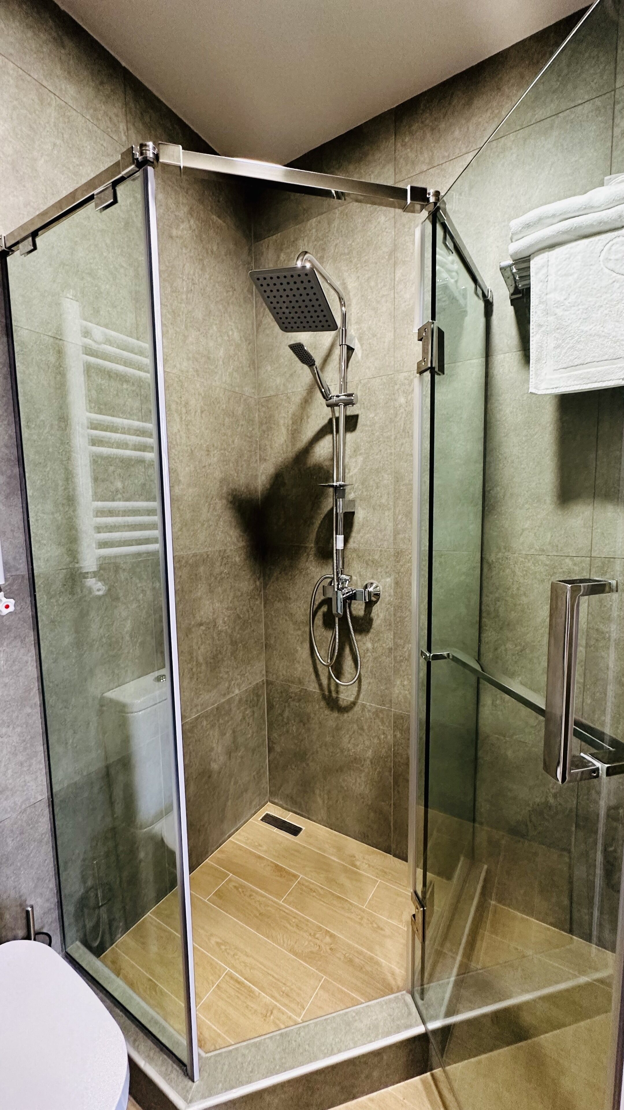 A glass-enclosed shower stall with a handheld showerhead, a handheld showerhead, and a wall-mounted faucet.