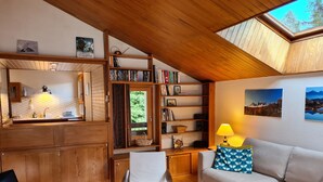 A cozy living area with a wooden ceiling, a bookshelf, a sofa, and a dining area with a window. - Apartment with view of Prorel (Briançon)