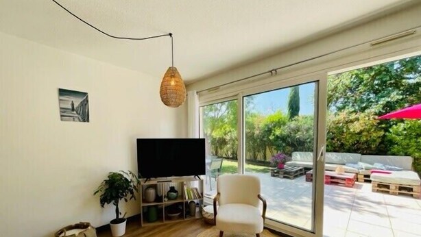 A living room with a TV, a chair, a plant, and a large sliding glass door leading to an outdoor patio. - Spacious cocoon with pool in La Rochelle (La Rochelle)