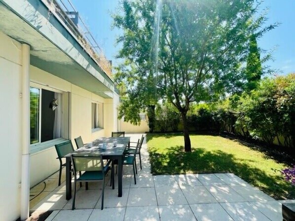 Un patio con una mesa, sillas, un árbol y un césped bien cuidado.