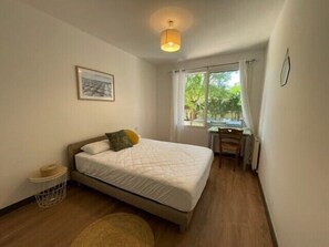 A bedroom with a bed, a desk, and a window with curtains.