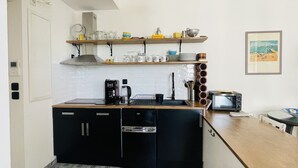 A compact kitchen with a black refrigerator, a coffee maker, and a toaster on the counter. There are shelves above the counter holding various kitchen items.