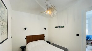 A bedroom with a wooden headboard, a white bedspread, a unique ceiling light, and a small bedside table.