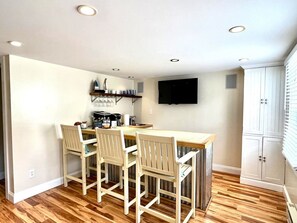 Eine Küche mit Holztisch und -stühlen, einer Kaffeemaschine und einem flachbildfernseher an der Wand.