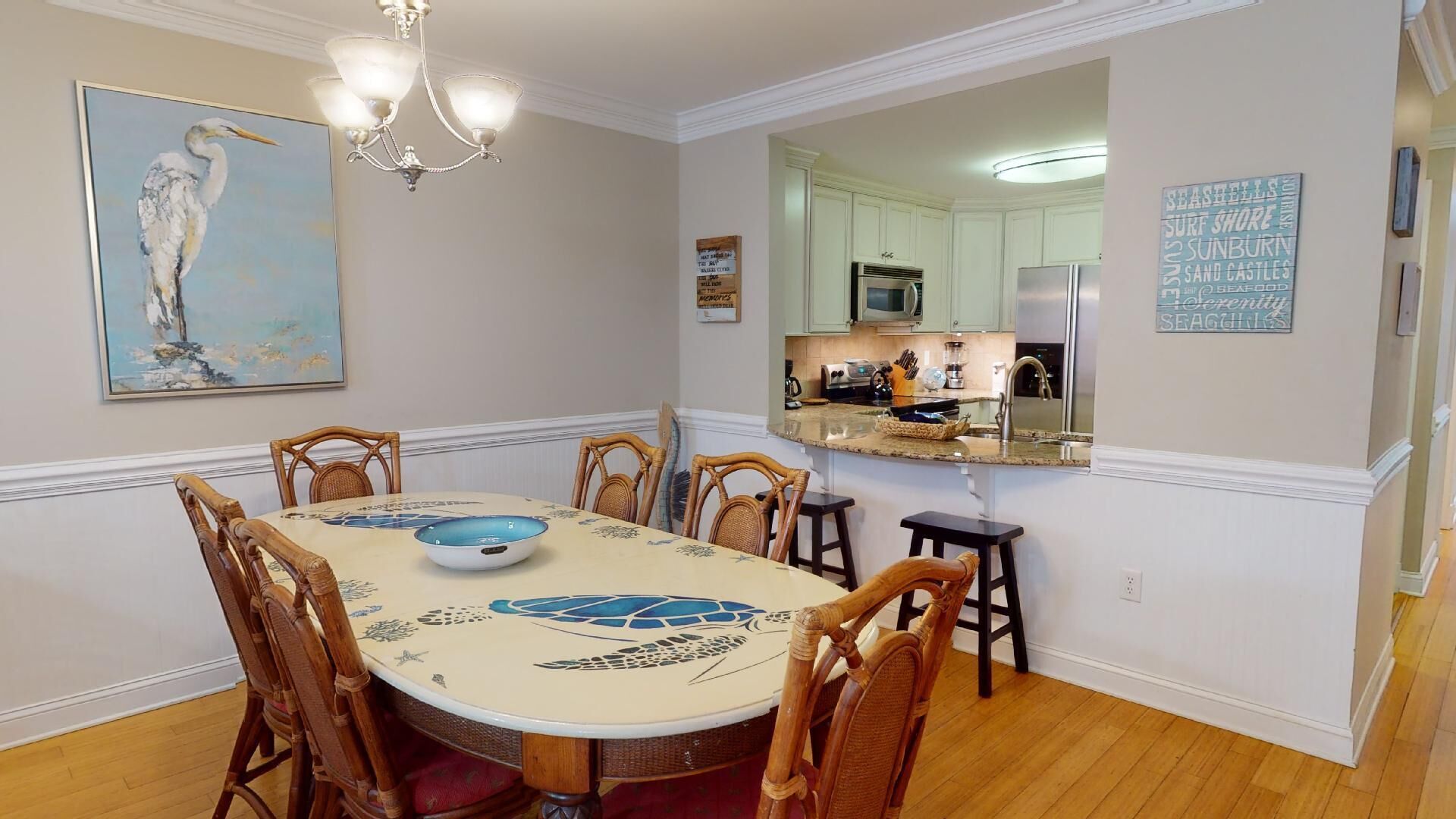 A dining area with a round table, chairs, a chandelier, and a painting of a bird.