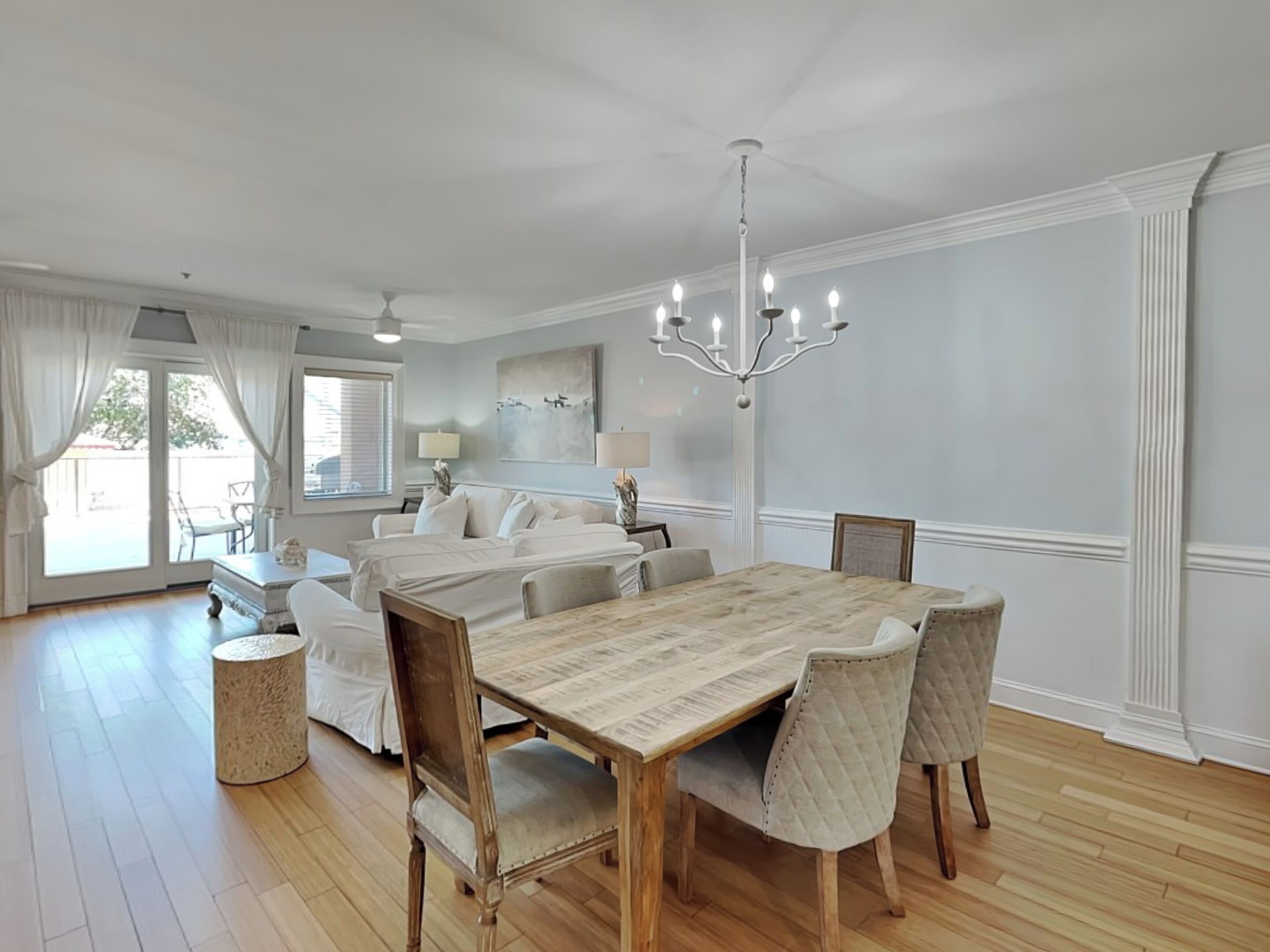 A spacious dining area with a wooden table and chairs, a chandelier, and a large window with curtains.