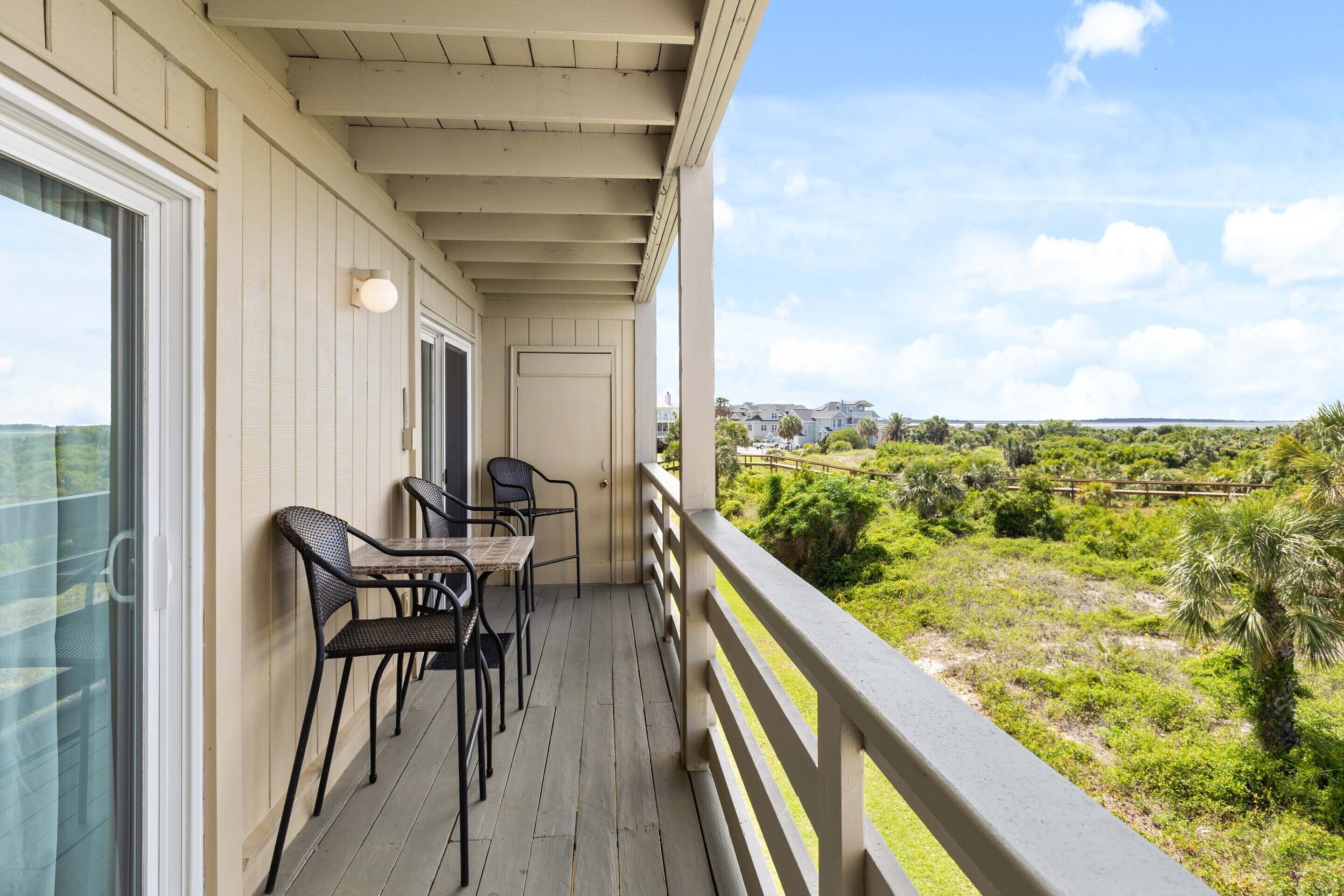 A balcony with a table and chairs, a view of greenery and distant buildings.