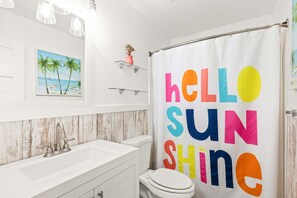 Un baño con un lavamanos blanco, un inodoro y una cortina de ducha con texto colorido.
