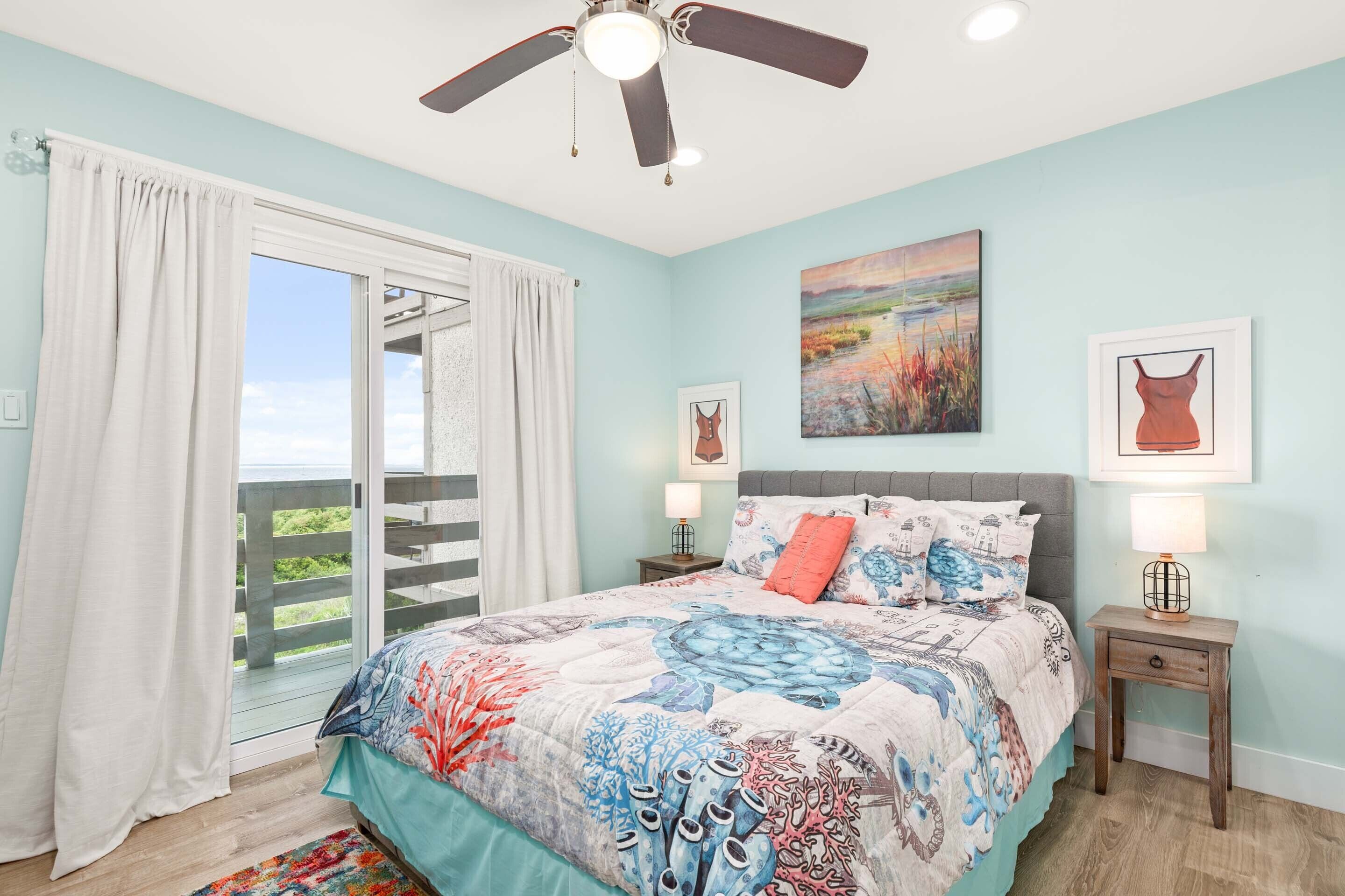 A bedroom with a large bed, a ceiling fan, a nightstand with a lamp, and a painting on the wall.