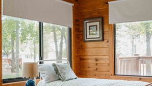 Una camera accogliente con un ventilatore a soffitto in legno, un letto con copriletto bianco, un tappeto rosso decorato e un comodino con una lampada.