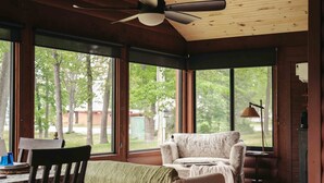 Una stanza accogliente con soffitto in legno, una ventola a soffitto, una grande finestra, un letto, una sedia e un tavolo.