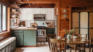 Una cucina accogliente con travi in legno, mobili bianchi, un'isola centrale e una zona pranzo con tavolo e sedie in legno.