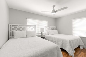 A bedroom with two beds, a ceiling fan, and a nightstand with a lamp.