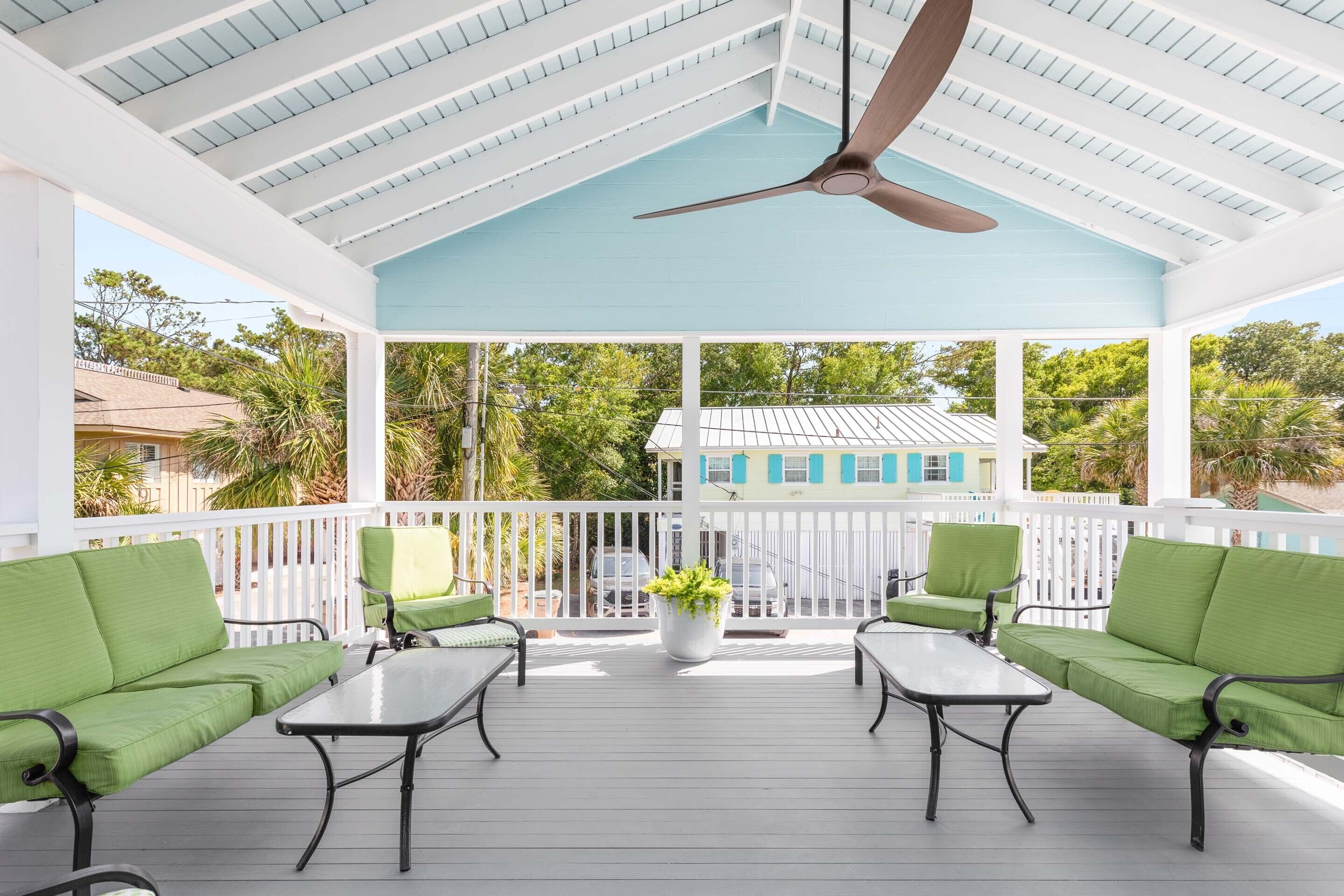 A covered outdoor area with a ceiling fan, green cushioned seating, and a potted plant.