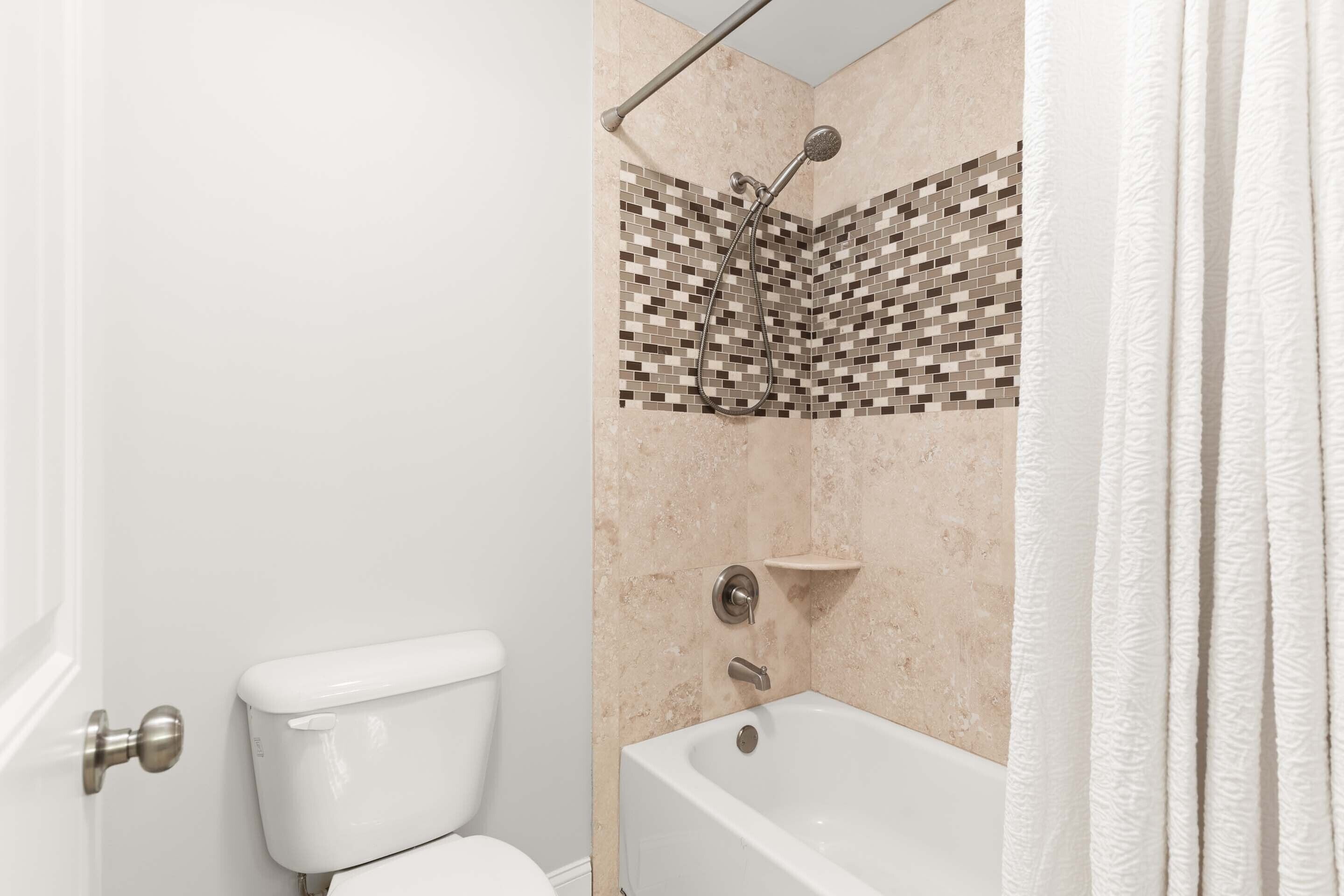 Une salle de bain comprenant des toilettes, une douche avec un mur carrelé et une baignoire.