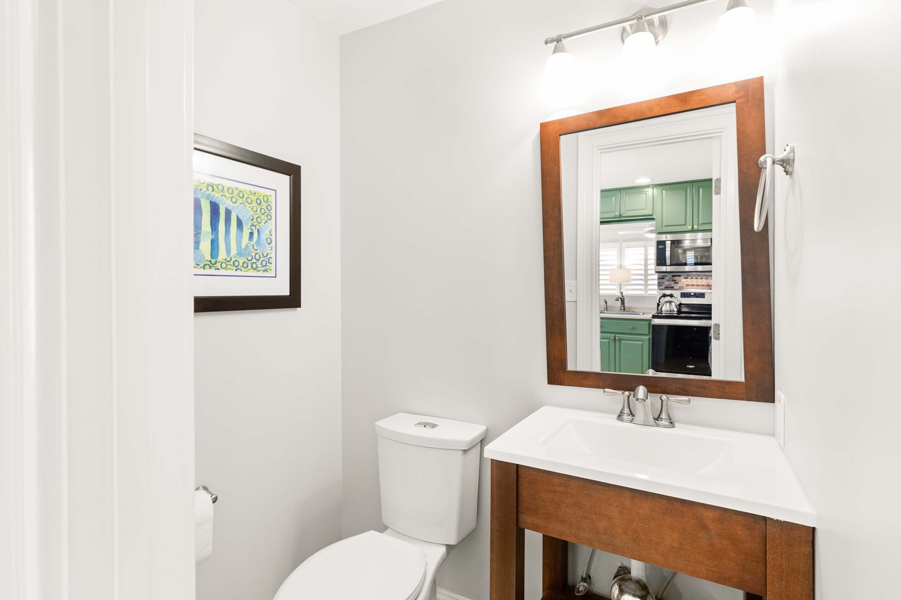 A bathroom with a white toilet, a wooden vanity with a white sink, and a framed mirror above the sink.
