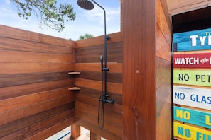 A wooden shower enclosure with a handheld showerhead and a sign with partially visible text. - Tybrisa Treasure by Tybee Vacation Rentals (Tybee Island)