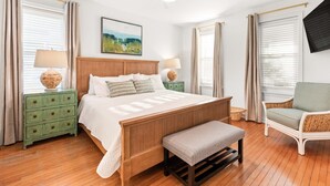A bedroom with a wooden bed, two nightstands with lamps, a bench, a chair, and a ceiling fan. - Tybrisa Treasure by Tybee Vacation Rentals (Tybee Island)