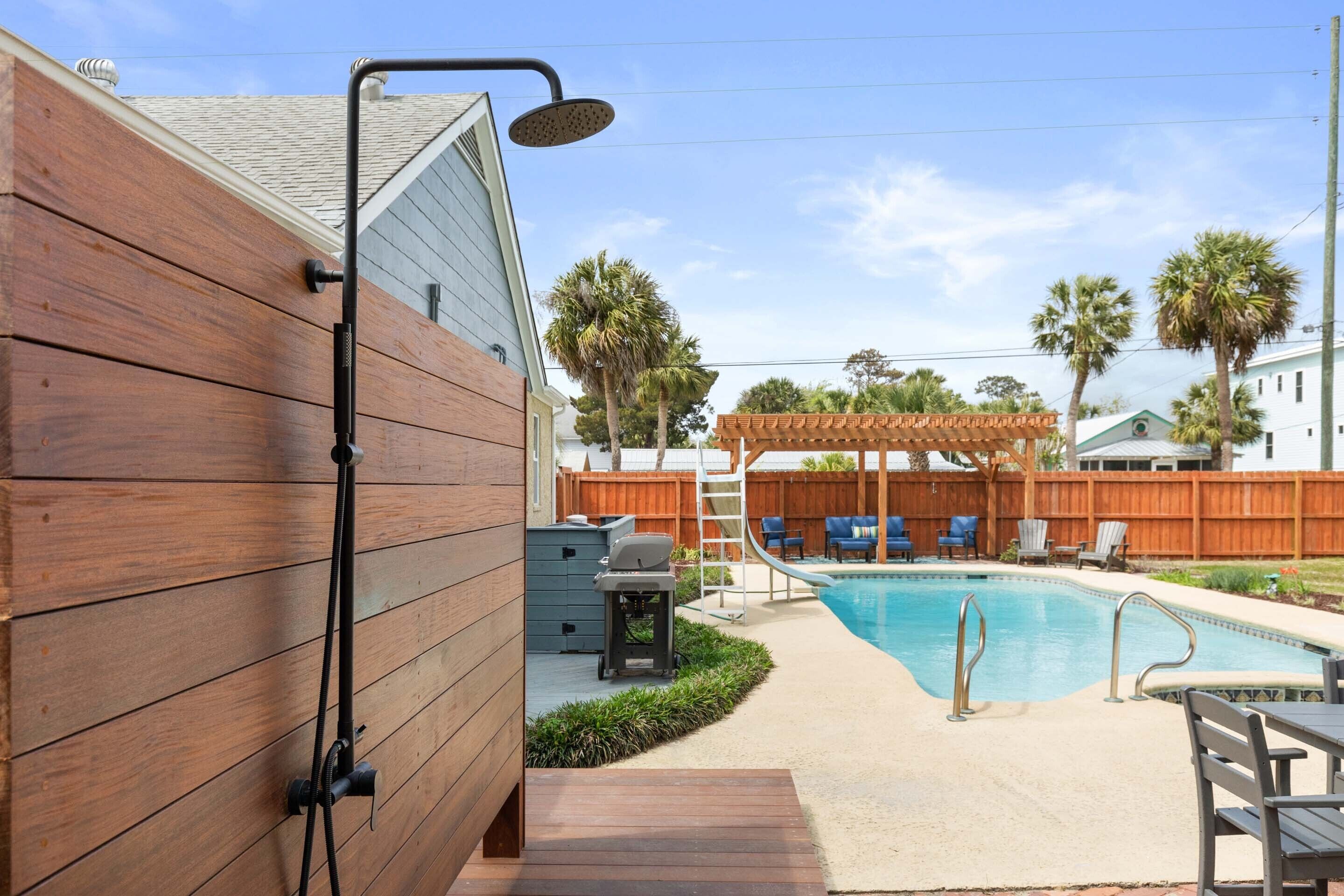 A backyard with a wooden deck, a pool, and a covered seating area.