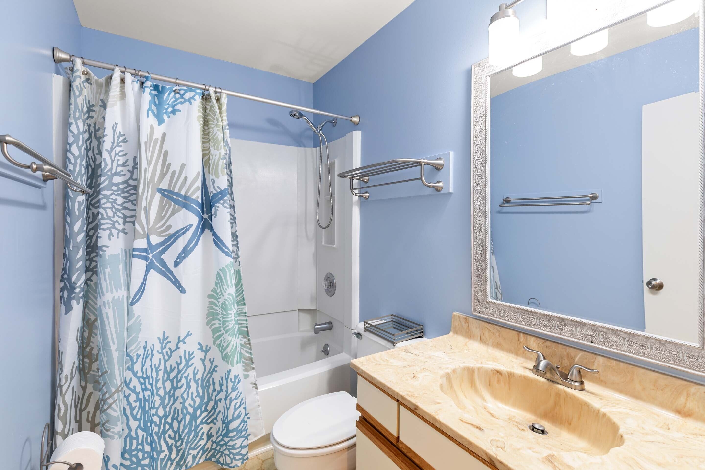 A bathroom with a shower curtain featuring a sea life pattern, a bathtub, a toilet, a sink with a mirror, and a towel rack.