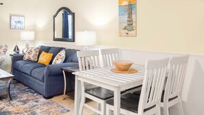 A living room with a blue sofa, white chairs, a small table, and a painting of a lighthouse. - Lighthouse Point 33A by Tybee Vacation Rentals (Tybee Island)