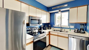 A modern kitchen with stainless steel appliances, wooden cabinets, and a blue accent wall. - Lighthouse Point 33A by Tybee Vacation Rentals (Tybee Island)