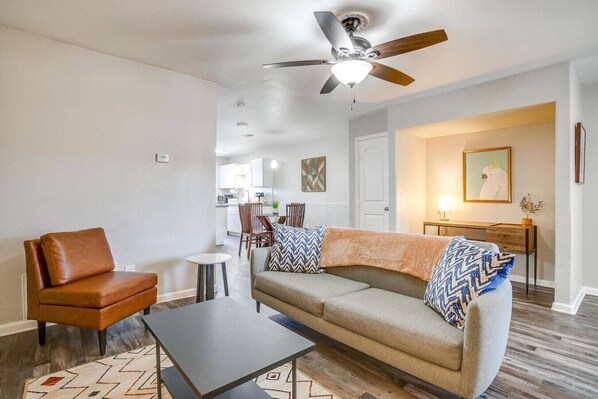A living room with a sofa, a coffee table, a leather chair, a ceiling fan, and a dining area in the background. - Beautiful 2 BR for Month Stay*Walk to UTA and Food (Arlington)