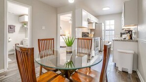 Une cuisine moderne avec des meubles blancs, une table à manger en verre et des chaises en bois.