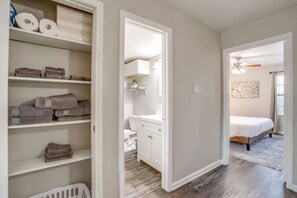 A bedroom with a bed, a bathroom with a toilet and sink, and a hallway with shelves. - Beautiful 2 BR for Month Stay*Walk to UTA and Food (Arlington)