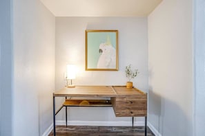 Uma mesa com uma luminária, uma planta e um quadro na parede.