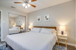 A hotel room with a large bed, a ceiling fan, two bedside lamps, and a mirror. - Beautiful 2 BR for Month Stay*Walk to UTA and Food (Arlington)