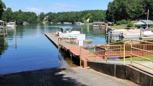 Un lac paisible où des bateaux sont amarrés à un quai, entouré d’arbres et d’un petit bâtiment.
