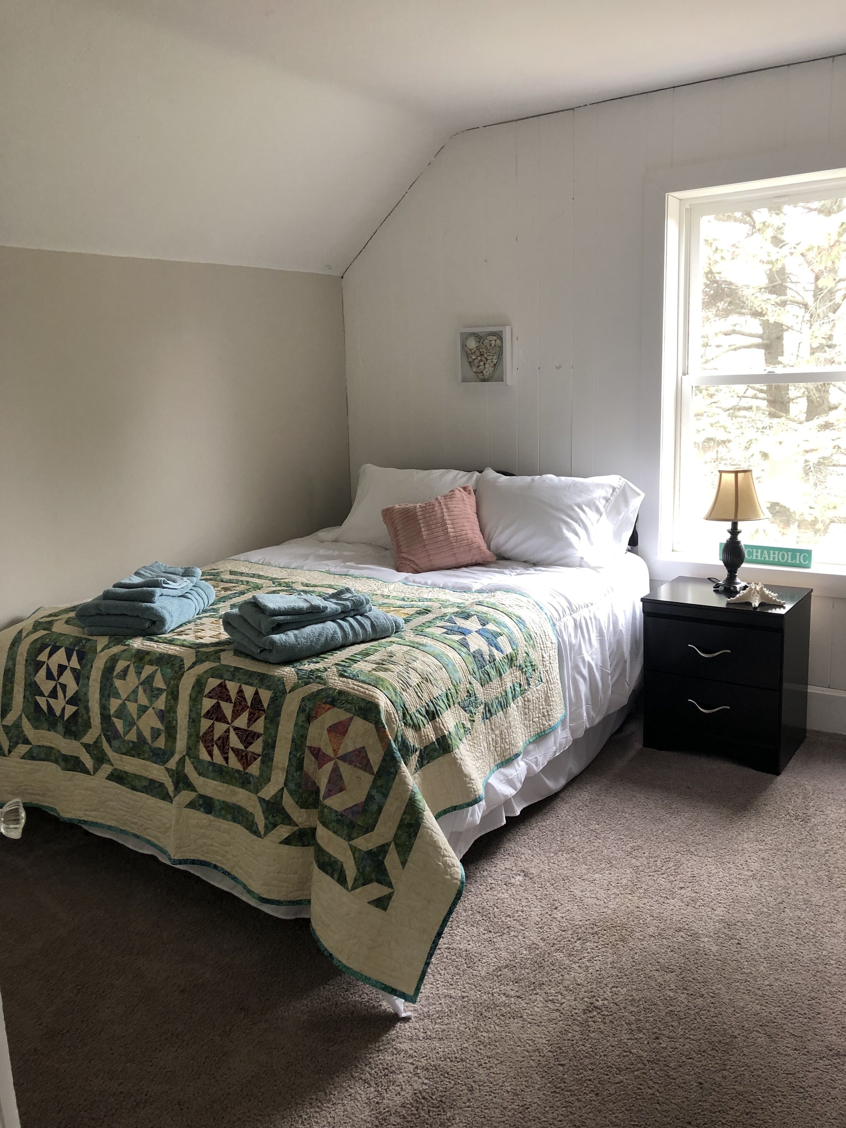 A bedroom with a bed, a nightstand, a lamp, and a window.