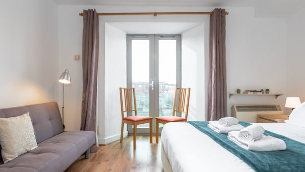 Habitación de hotel con cama, sofá, dos sillones, lámpara y vistas por la ventana.