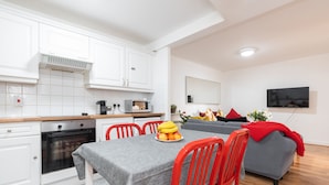 Una cocina moderna con armarios blancos, horno empotrado y un comedor con mesa y sillas.