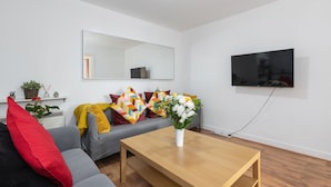 Una sala de estar moderna con un sofá gris, una mesa de centro de madera y un televisor de pantalla plana montado en la pared.