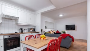 Una cocina moderna con armarios blancos, encimera de madera y zona de comedor con mesa de madera y sillas rojas.