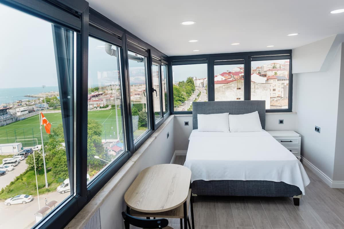 A modern bedroom with a large bed, a small table, and a view of the city through large windows.