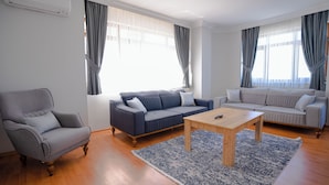 A modern living room with a grey armchair, a blue sofa, and a light-colored sofa. A wooden coffee table is in the center. - Grand Family Home (Trabzon)