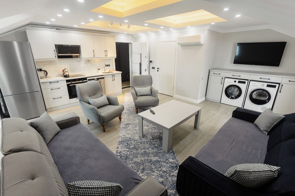 A modern living room with a sofa, armchairs, a coffee table, and a TV.
