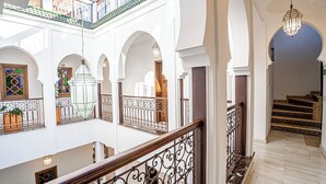 Un interior de varios niveles con corredores en arco, una escalera de madera y barandillas de metal decorativo.